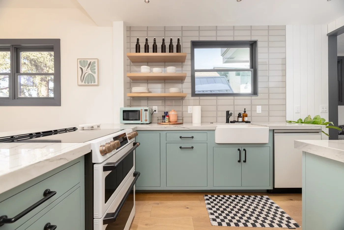 Una cocina luminosa con gabinetes verde claro, encimeras blancas y estantes abiertos.