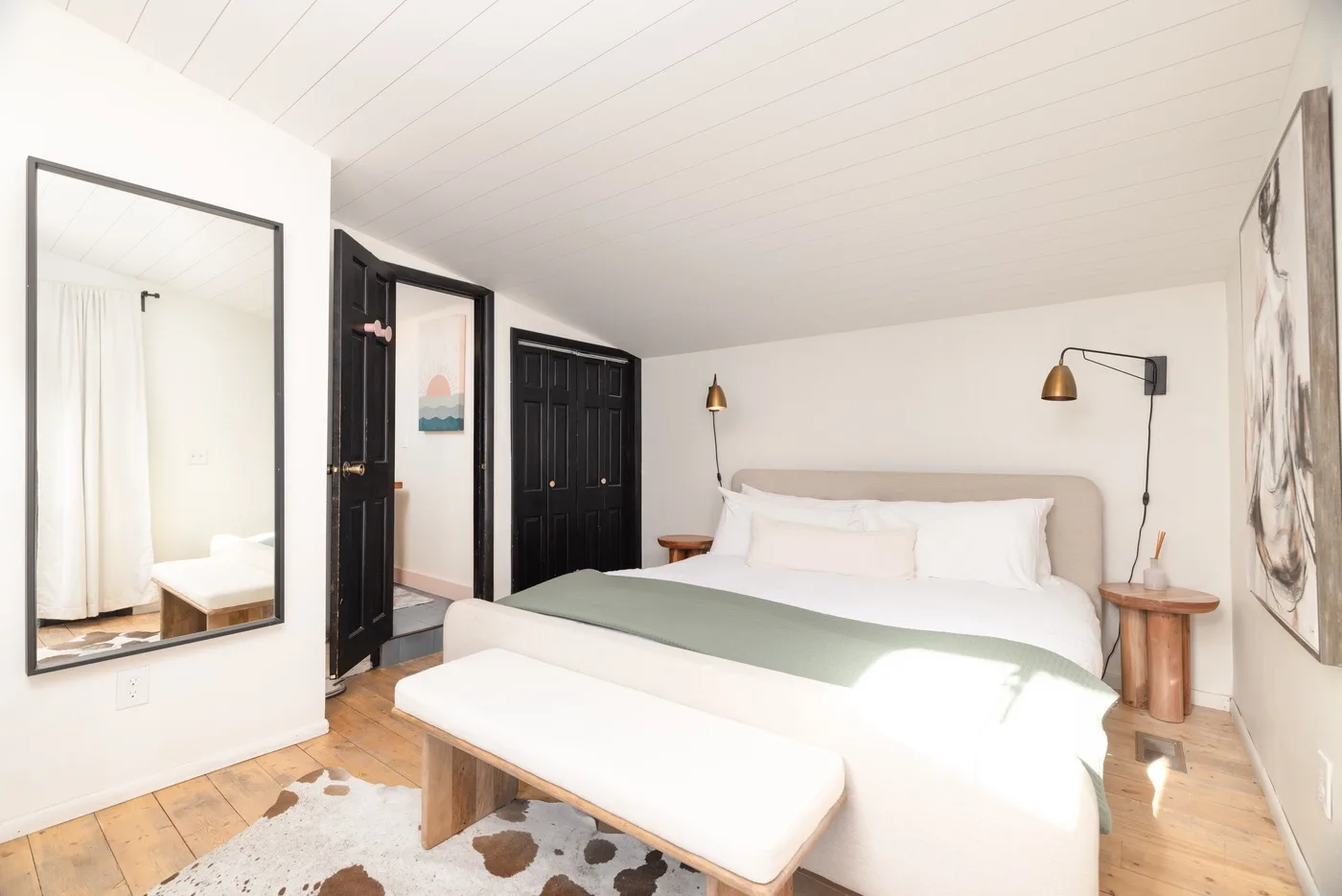 Un dormitorio luminoso con una cama grande, un banco y suelo de madera clara.