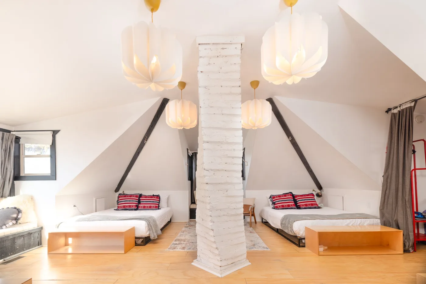 Un dormitorio abuhardillado luminoso con dos camas bajo techos inclinados y lámparas colgantes.