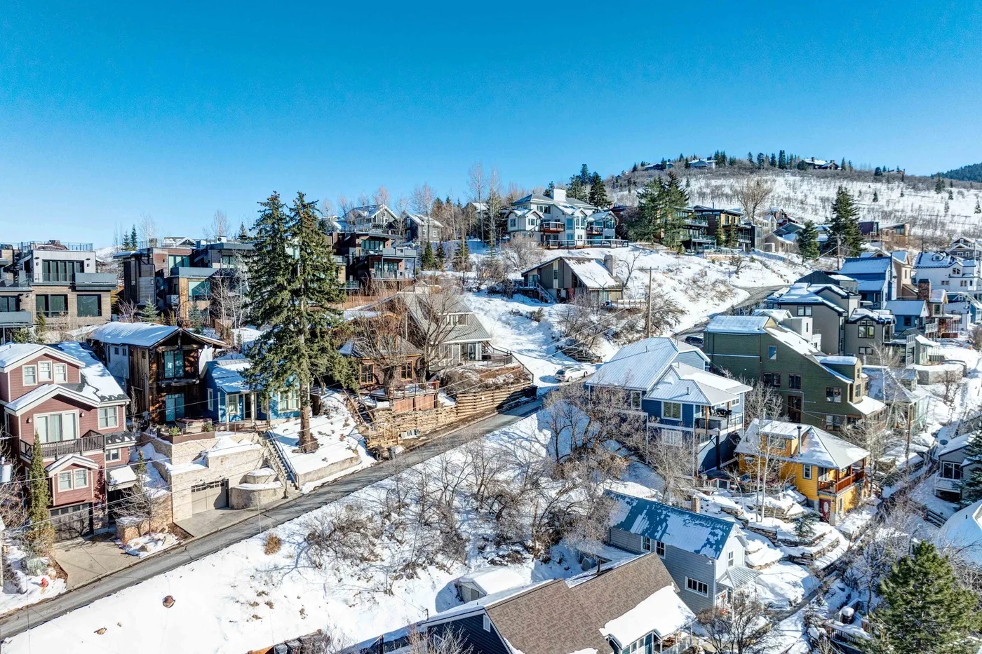 Un barrio residencial nevado se extiende por una ladera bajo un cielo azul despejado.