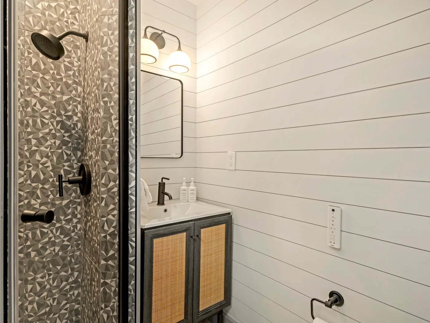 Un baño con una pared de ducha estampada y un mueble de lavabo.