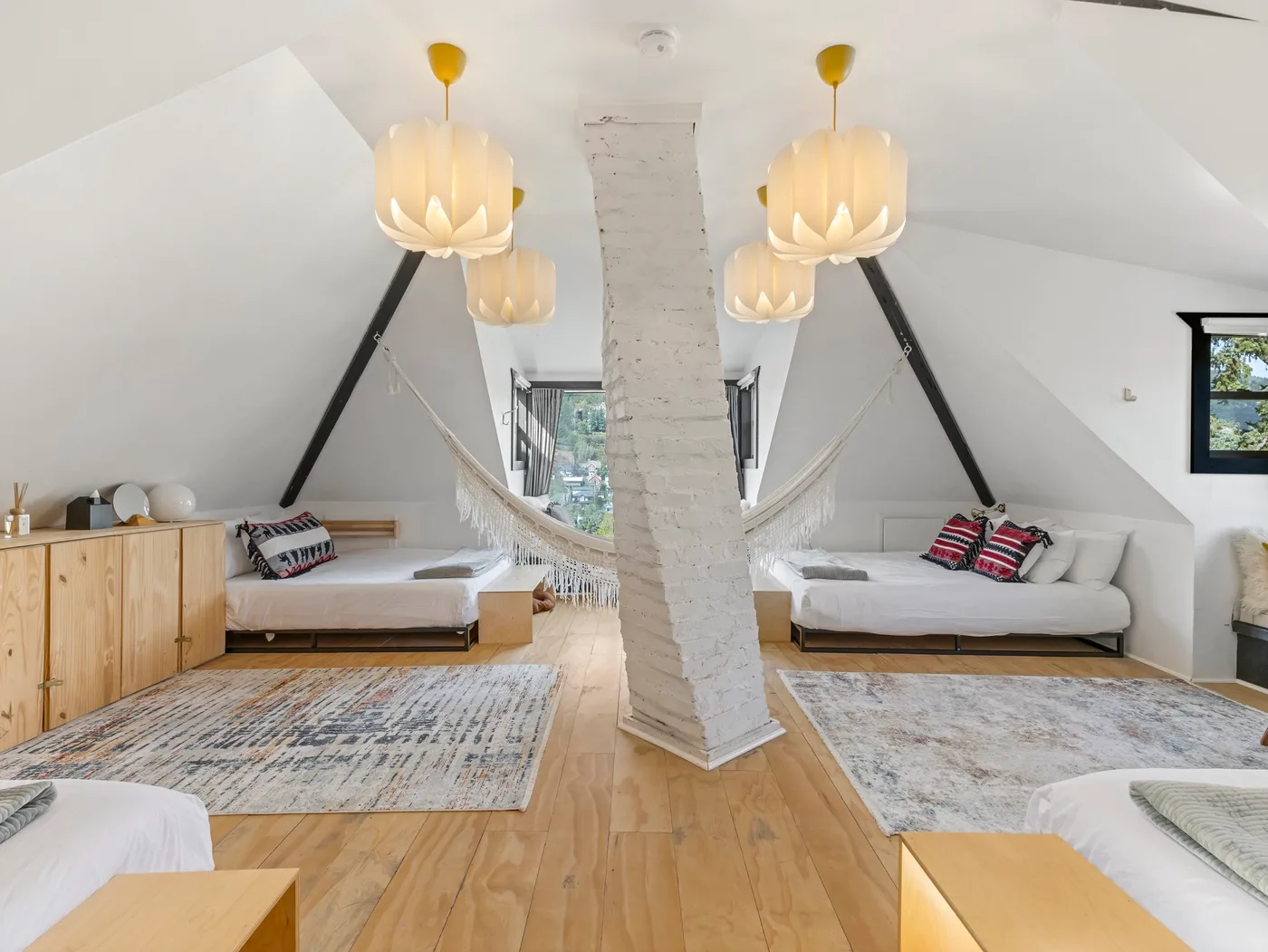Un dormitorio abuhardillado luminoso con camas, una columna central y una hamaca colgante.