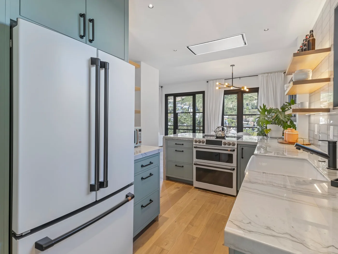Una cocina luminosa con un refrigerador grande, una estufa central y encimeras blancas.