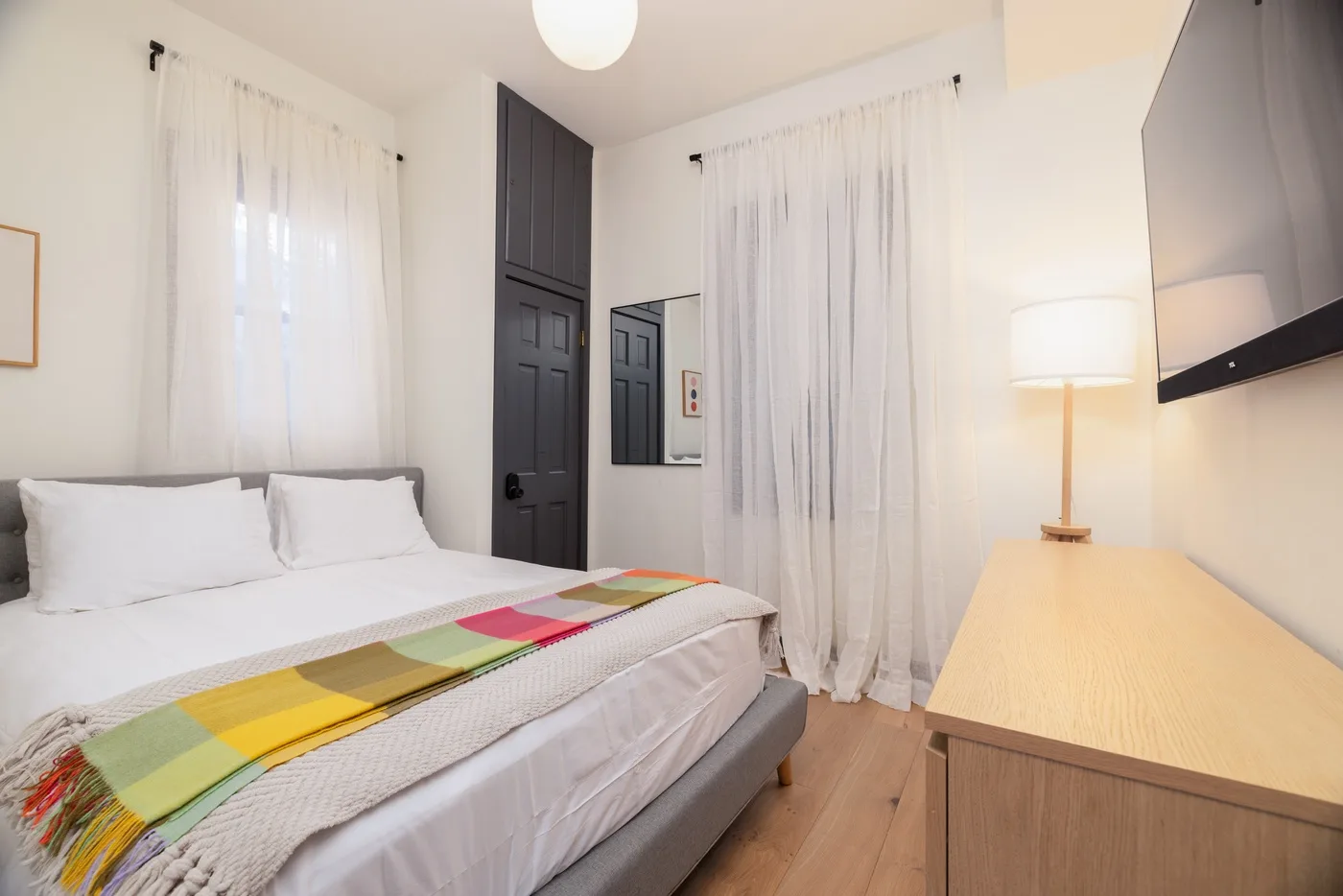 Un dormitorio con una cama bien hecha, una mesa auxiliar y cortinas claras.