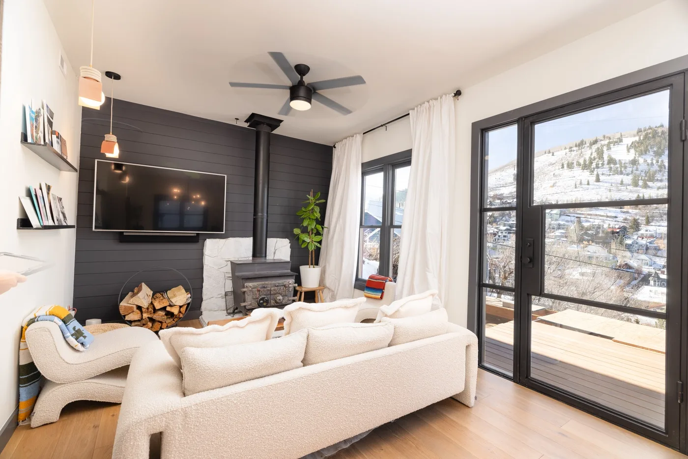 Una sala luminosa con asientos, un televisor y grandes ventanas con vistas a una ladera nevada.