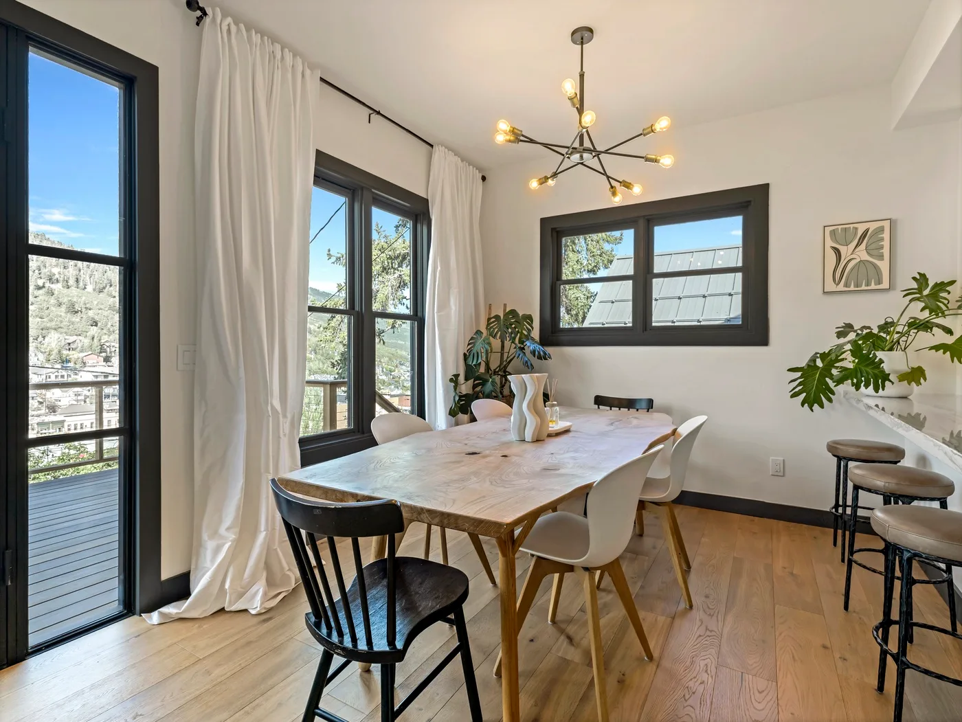 Un comedor luminoso con una mesa de madera, ventanas amplias y plantas en macetas.
