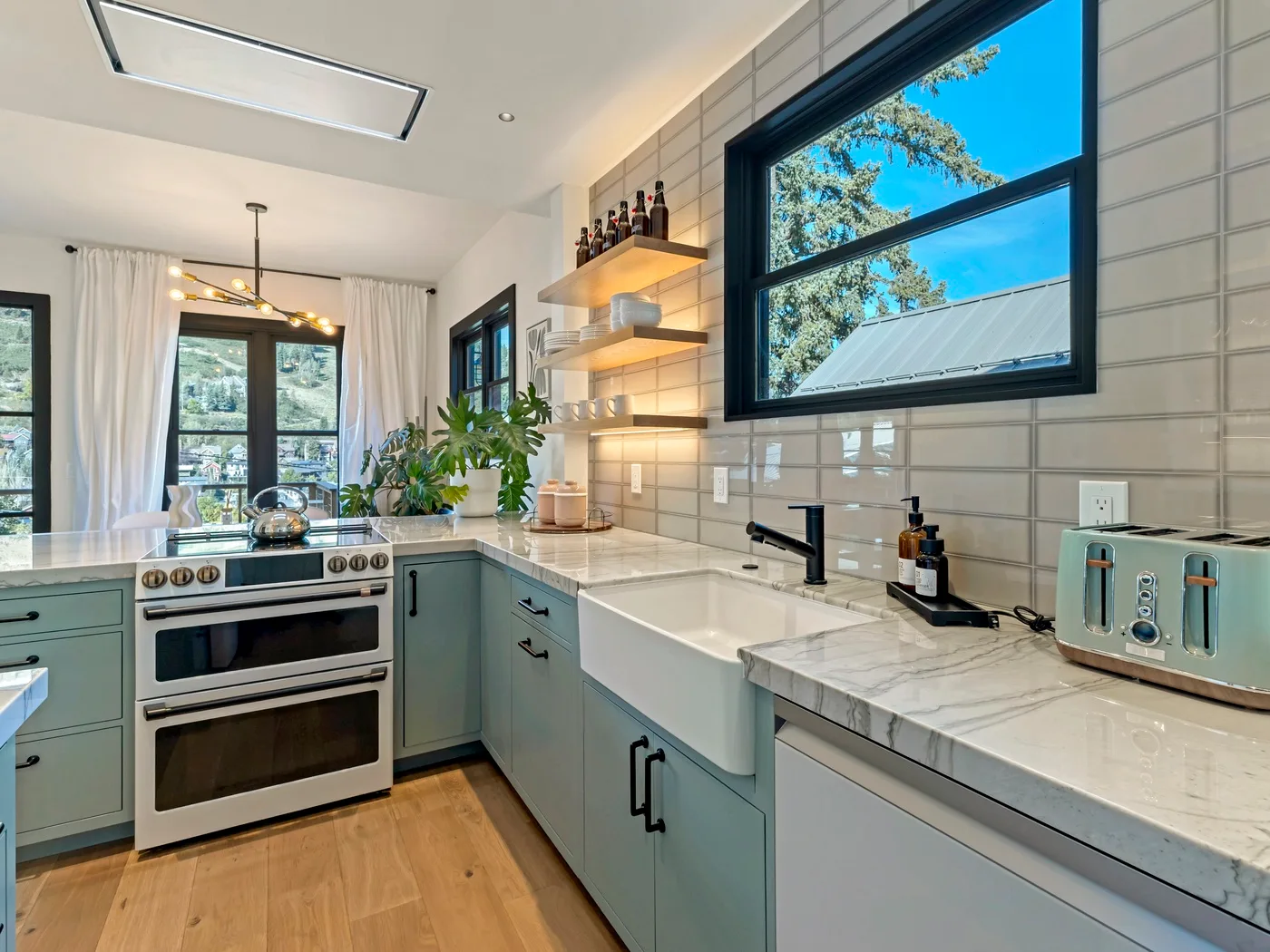 Una cocina luminosa con gabinetes verde claro, un fregadero amplio y una ventana grande.