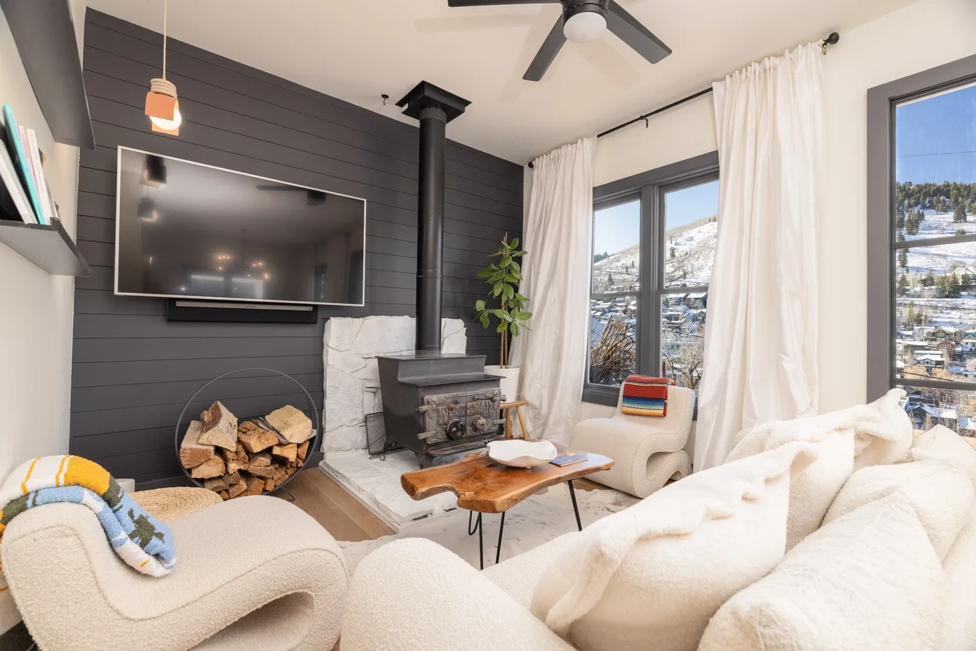 A bright living room with a fireplace, television, and large windows overlooking a snowy landscape.