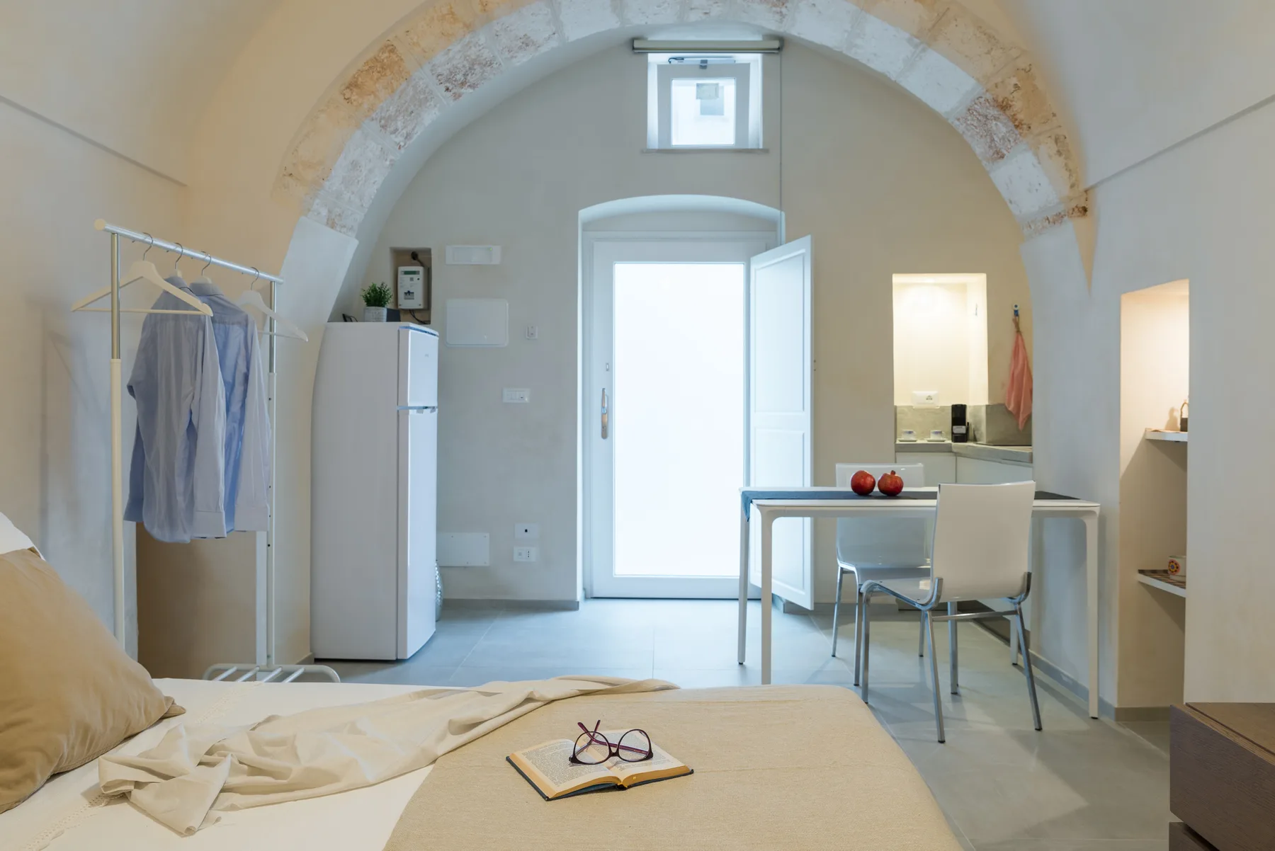 Un dormitorio luminoso con una cama, una pequeña mesa de comedor y techo abovedado.