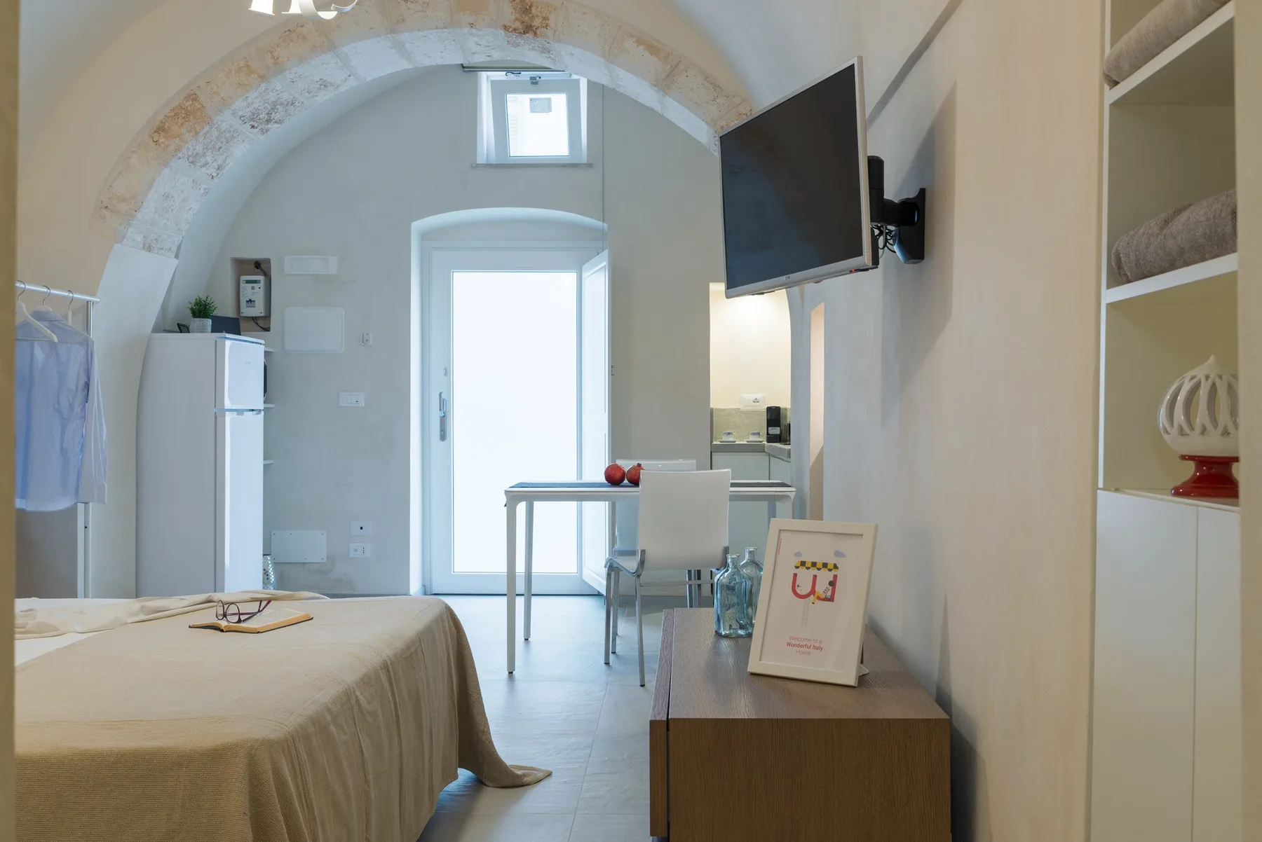 Un dormitorio con cama, mesa de comedor y televisor bajo un techo abovedado.