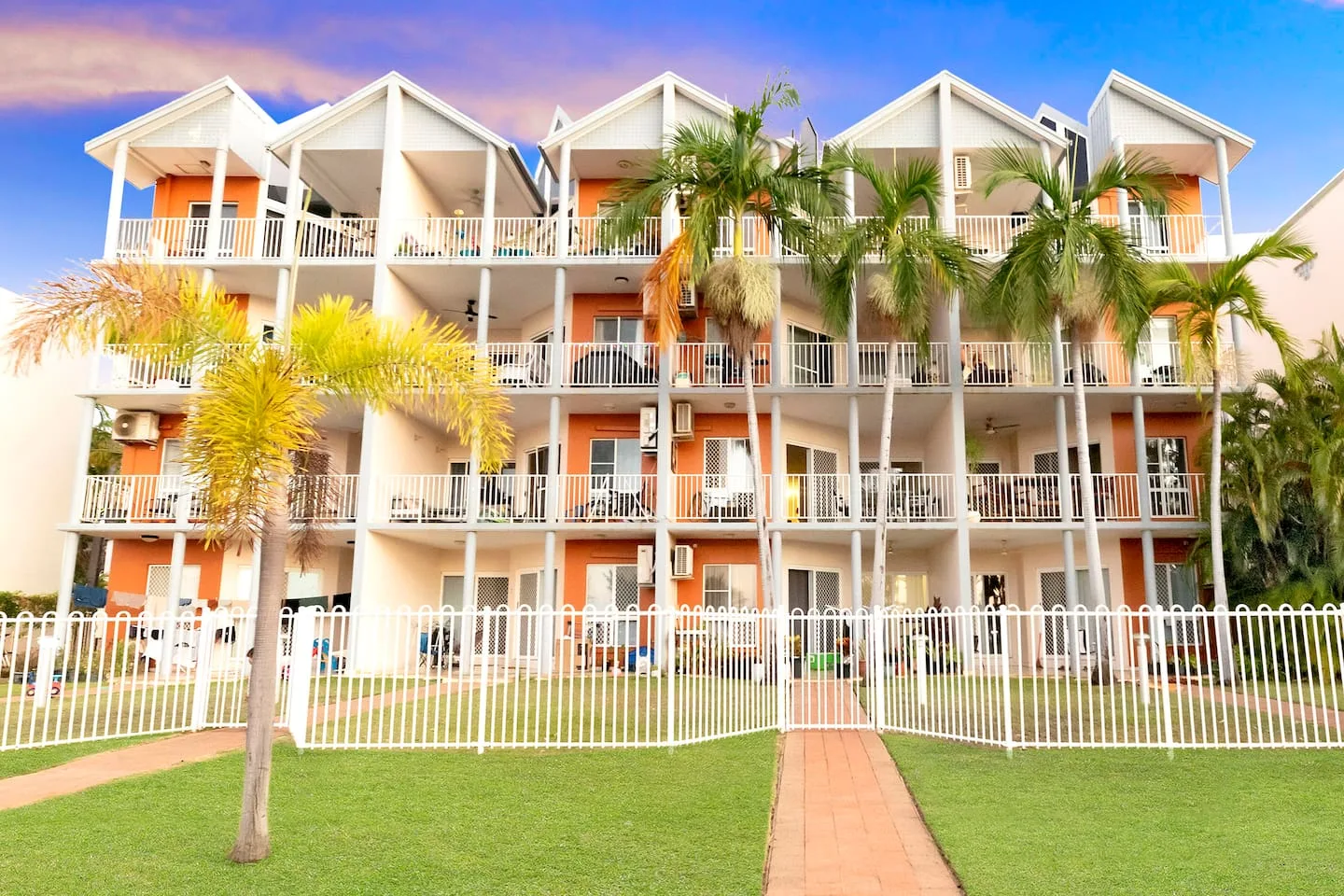 A multi-story building with balconies stands behind a lawn and paved walkway.