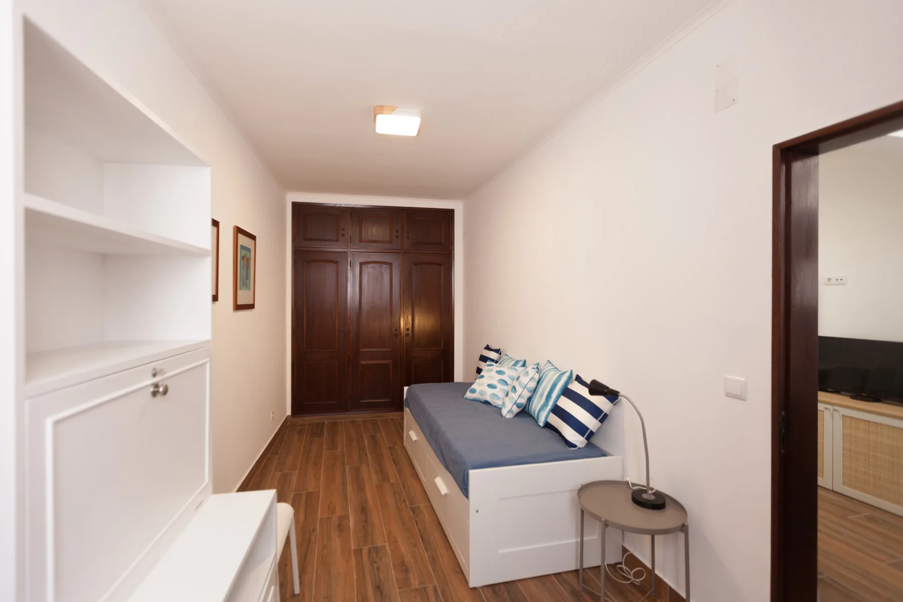 Un dormitorio estrecho con una cama individual, estanterías empotradas y suelo de madera.