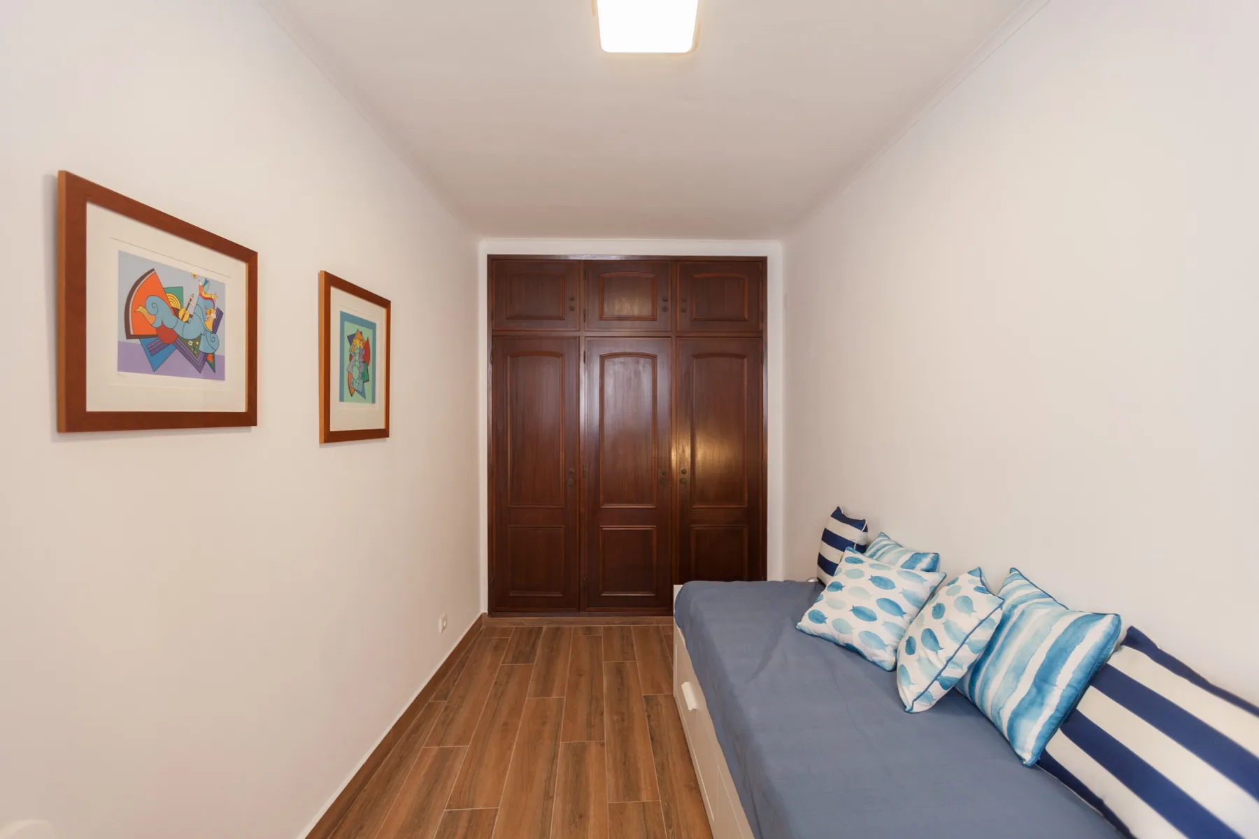 Un dormitorio estrecho tiene una cama con ropa de cama azul y blanca y un armario de madera.