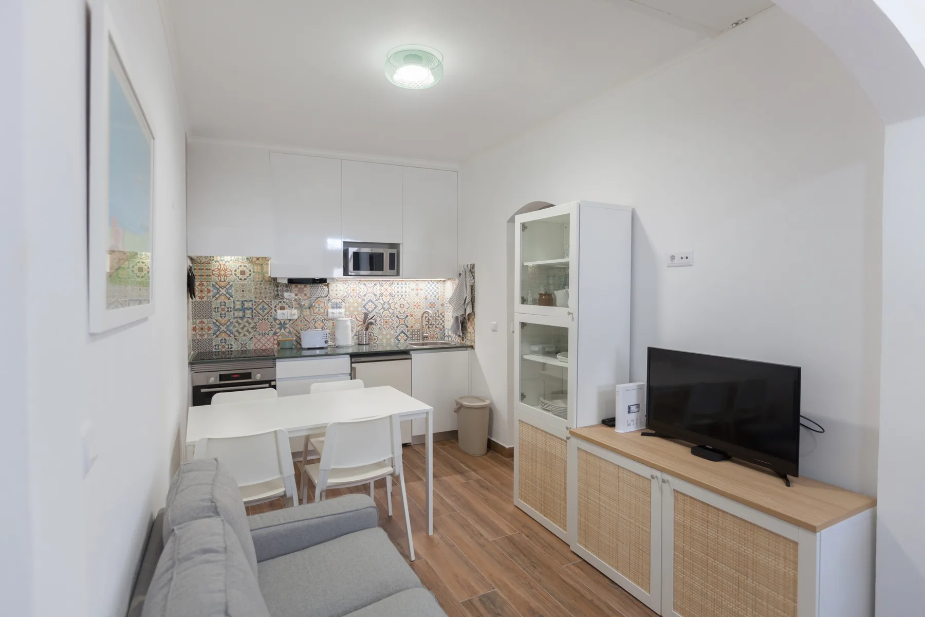 Una sala luminosa con televisor, asientos y cocina integrada.