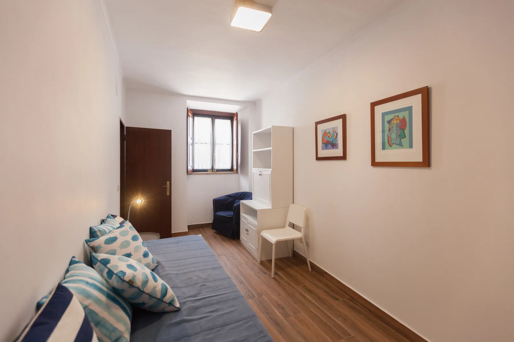 Dormitorio con una cama, una silla y cuadros enmarcados en la pared.