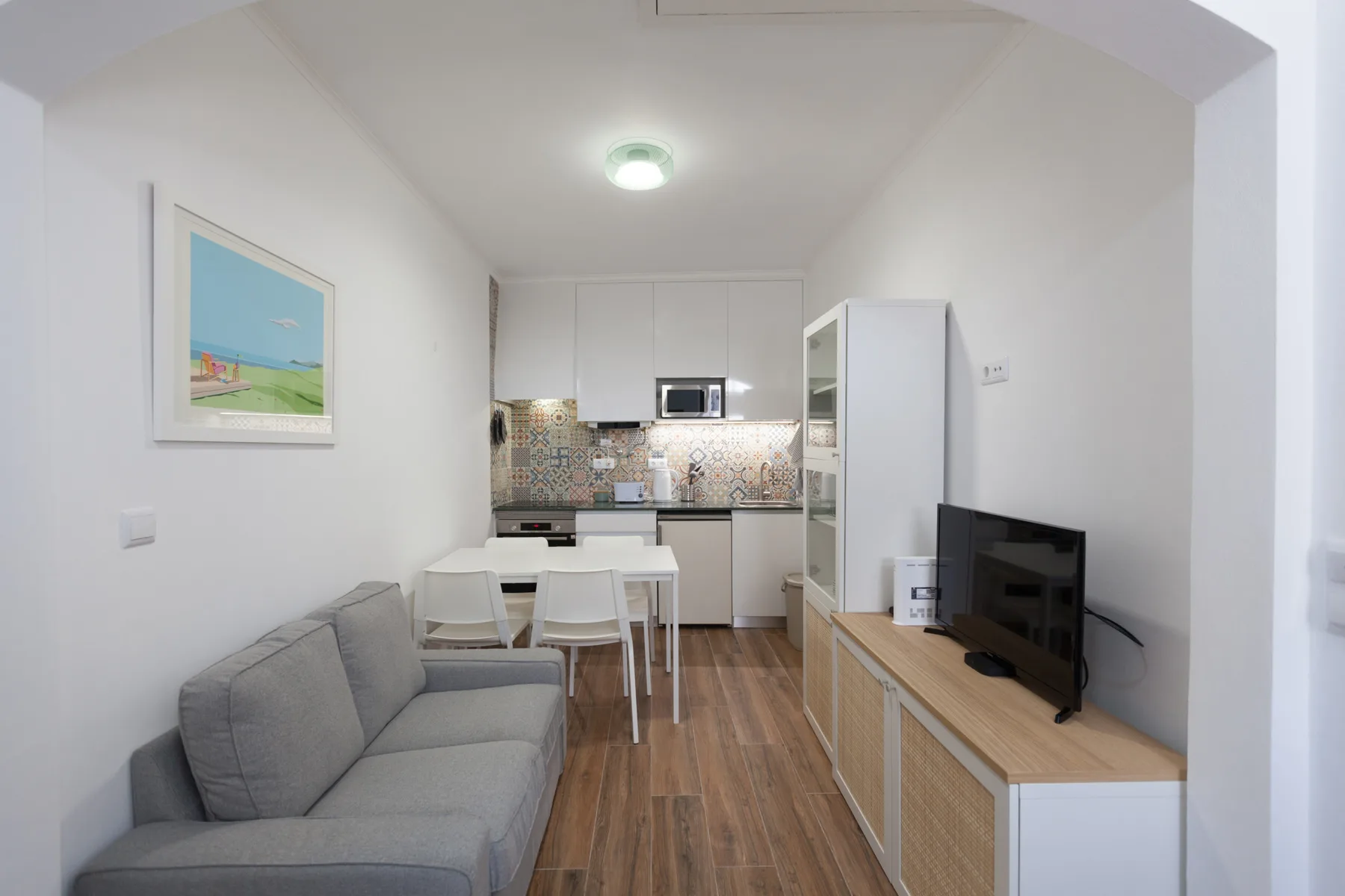 Una luminosa sala de estar con sofá gris, mesa de comedor y cocina abierta.