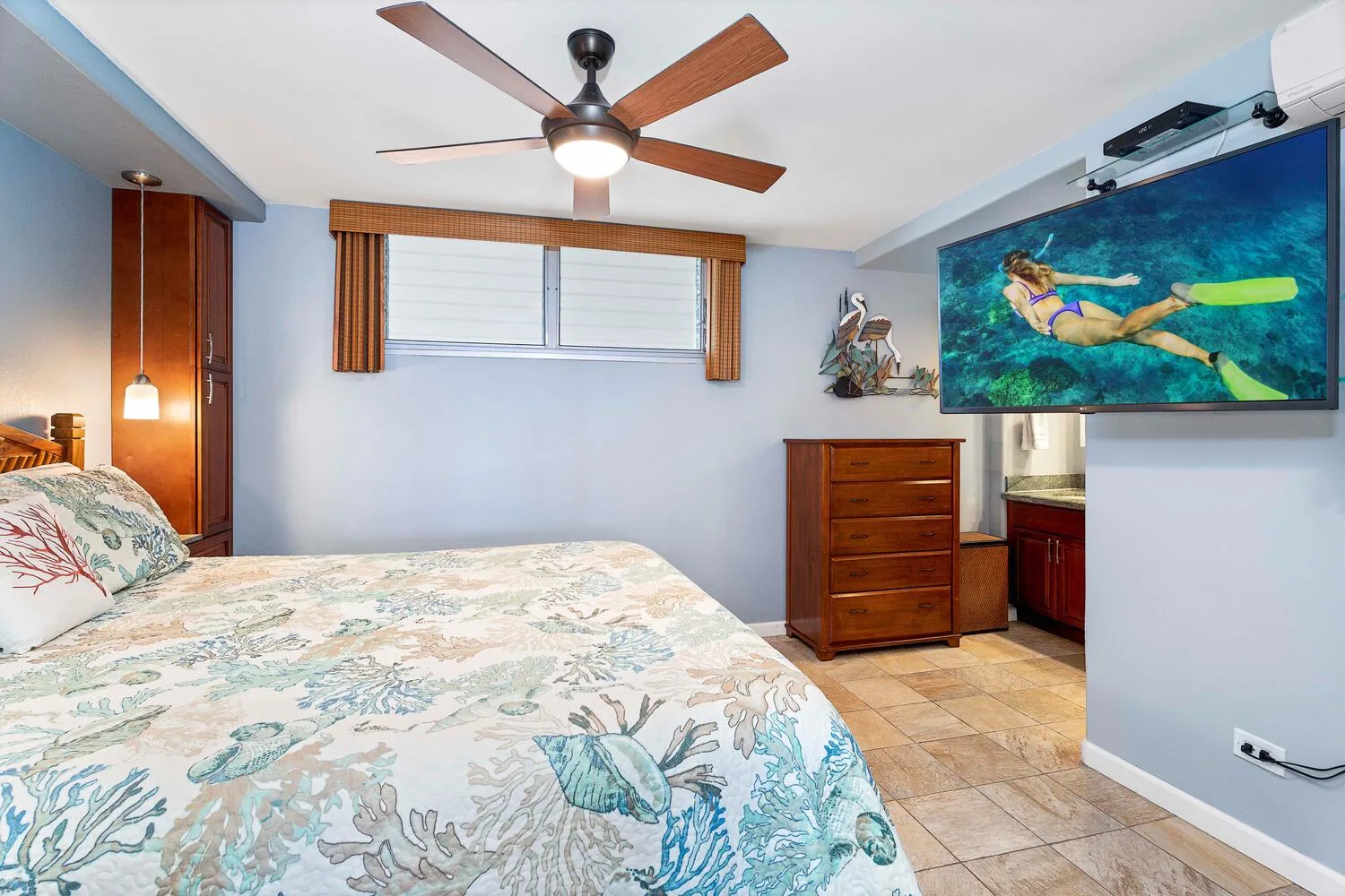 Un dormitorio con una cama, una cómoda y un televisor que muestra una escena submarina.