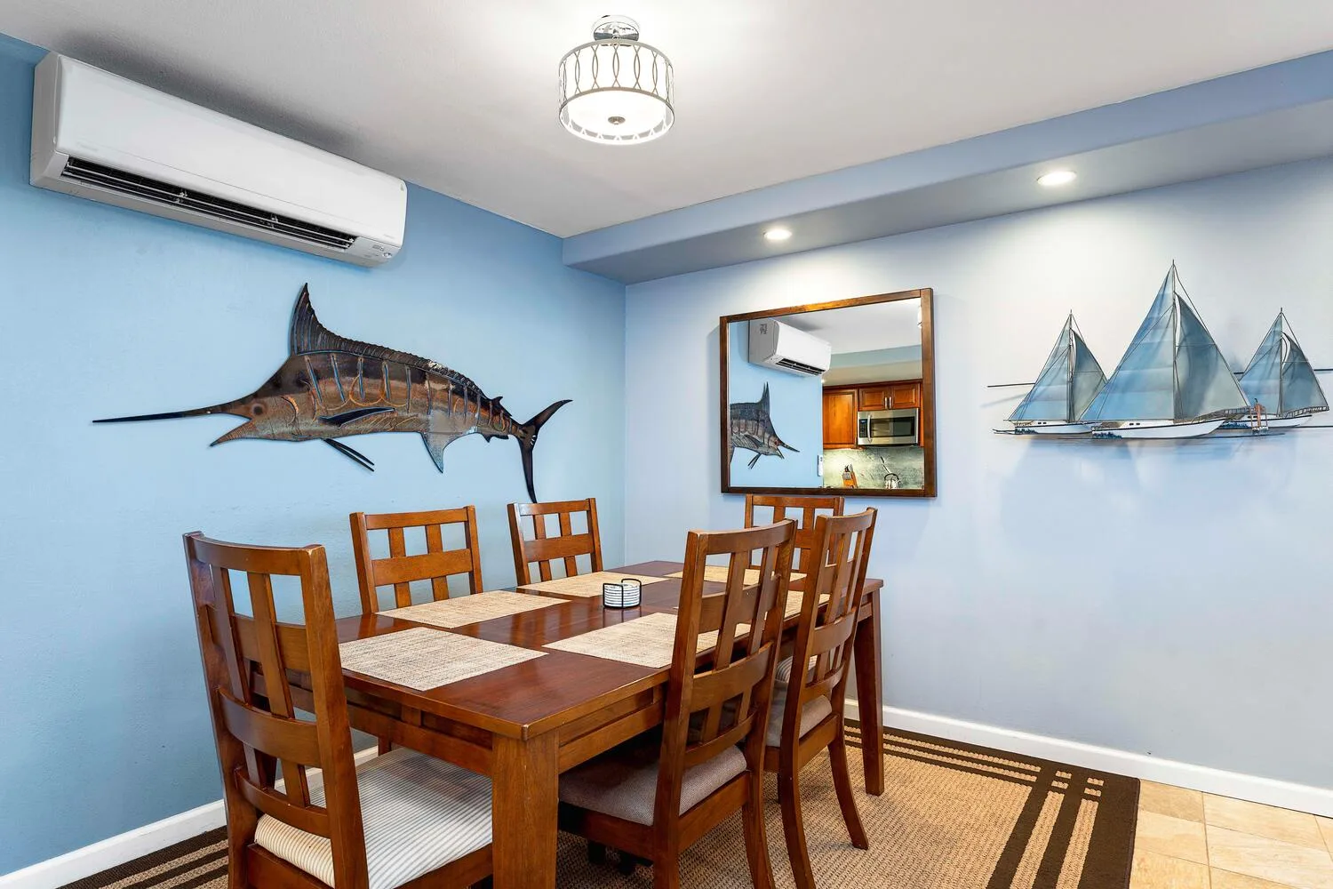 Un comedor con una mesa y sillas de madera bajo adornos marinos en la pared.