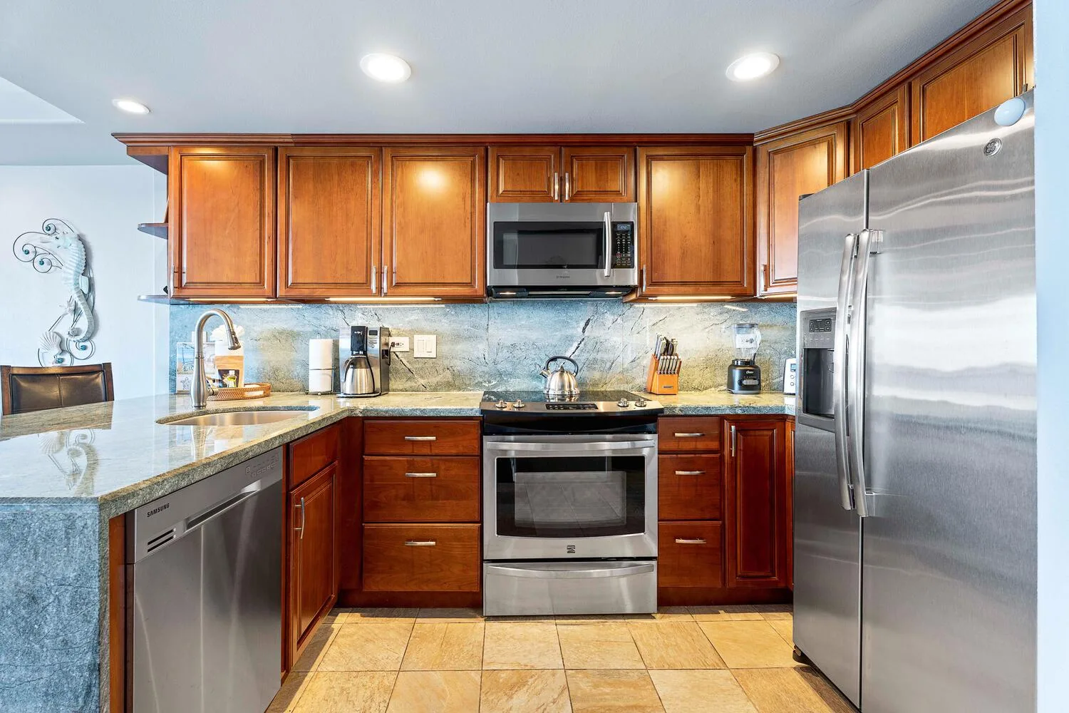 Una cocina con gabinetes de madera, encimeras de piedra y electrodomésticos de acero inoxidable.