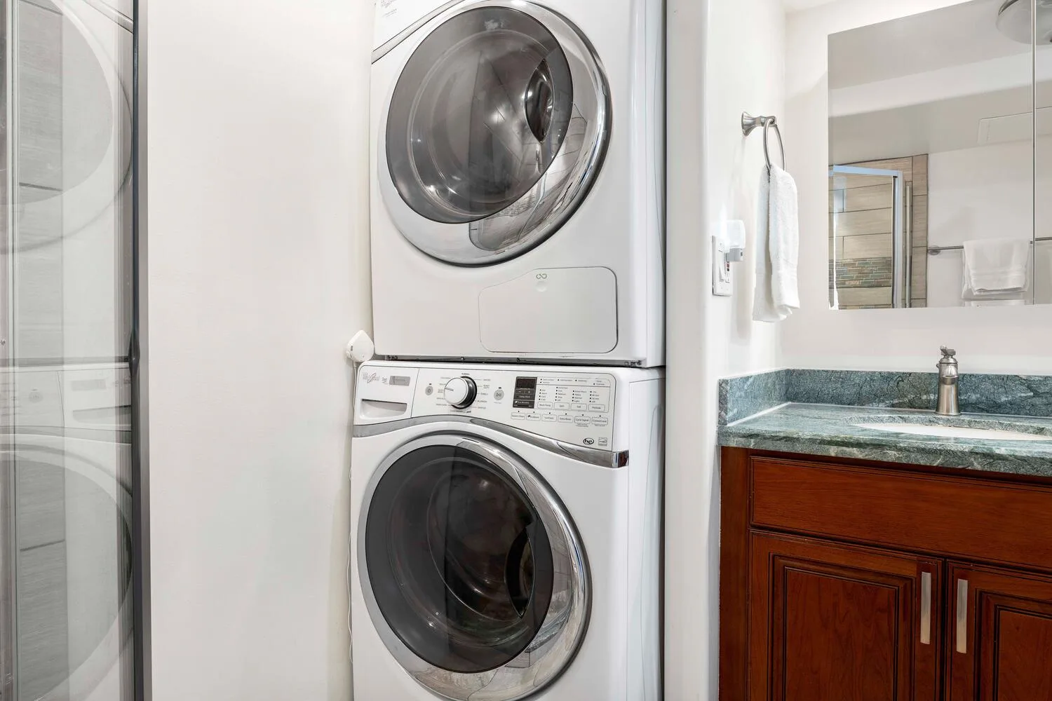 Un baño con una lavadora y secadora apiladas junto a un lavabo y un espejo.