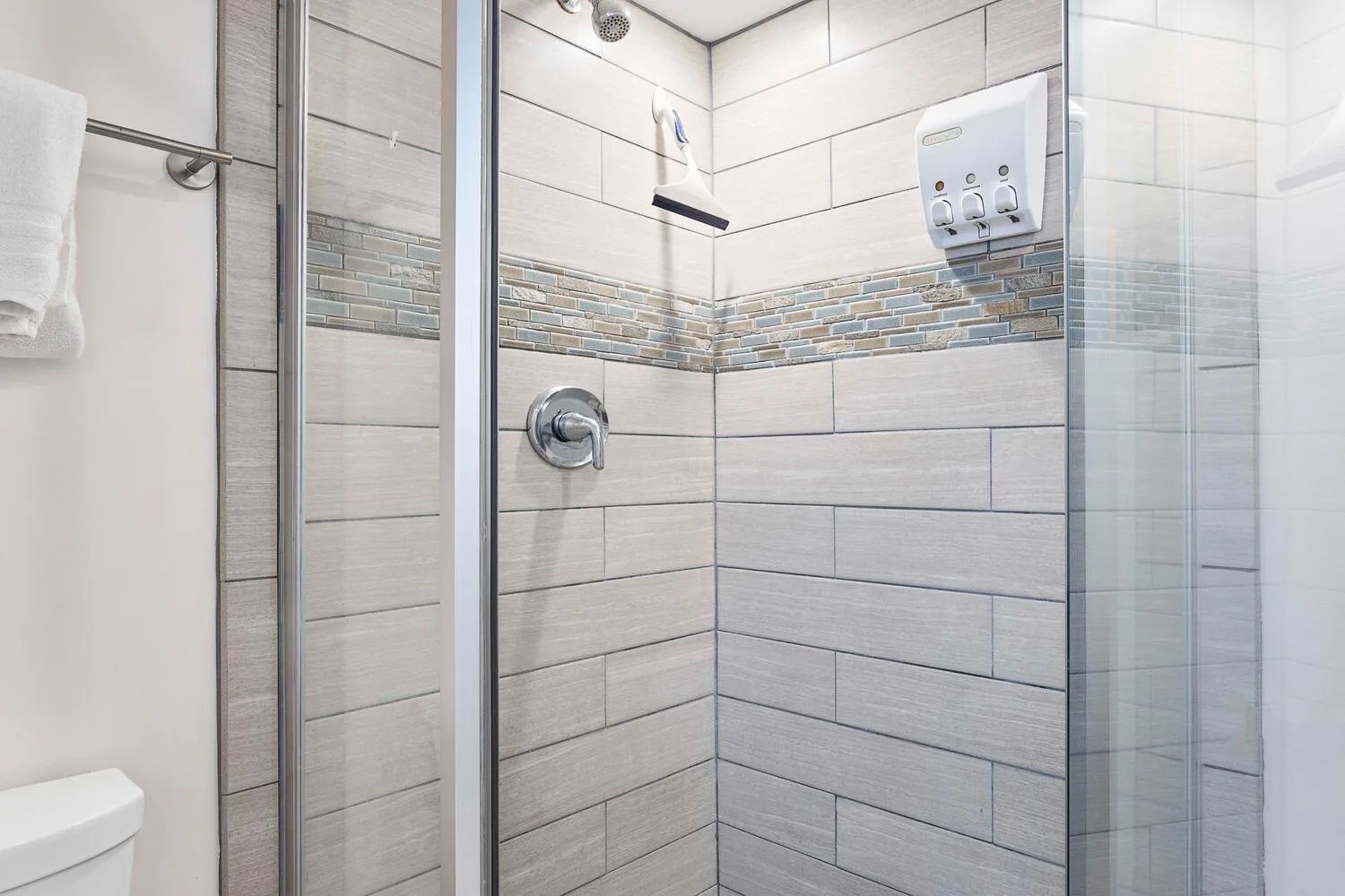 Una zona de ducha con azulejos, mampara de vidrio y controles en la pared.