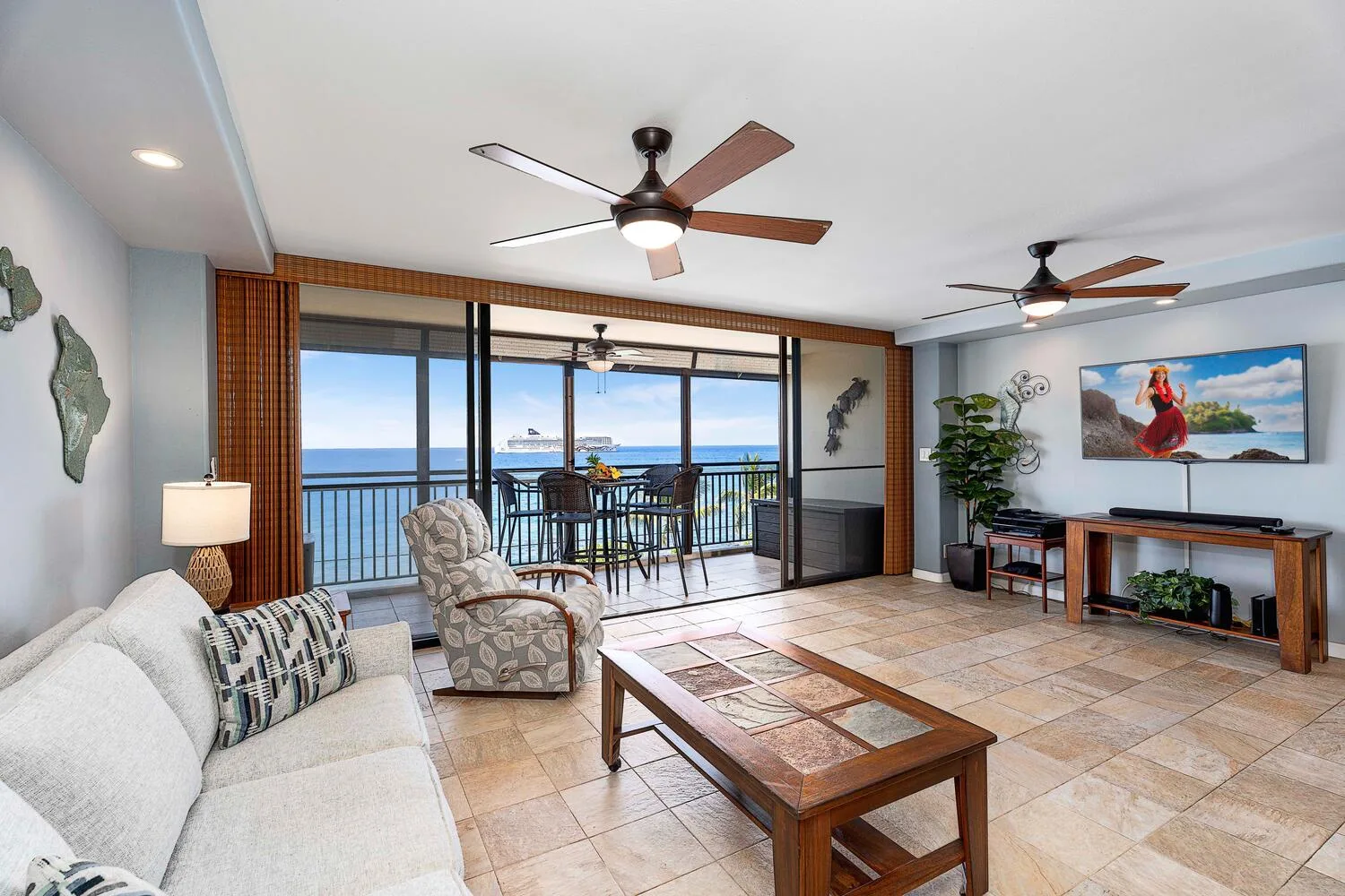 Una sala de estar con asientos y una mesa de centro de vidrio, abierta a un balcón con vistas al mar.