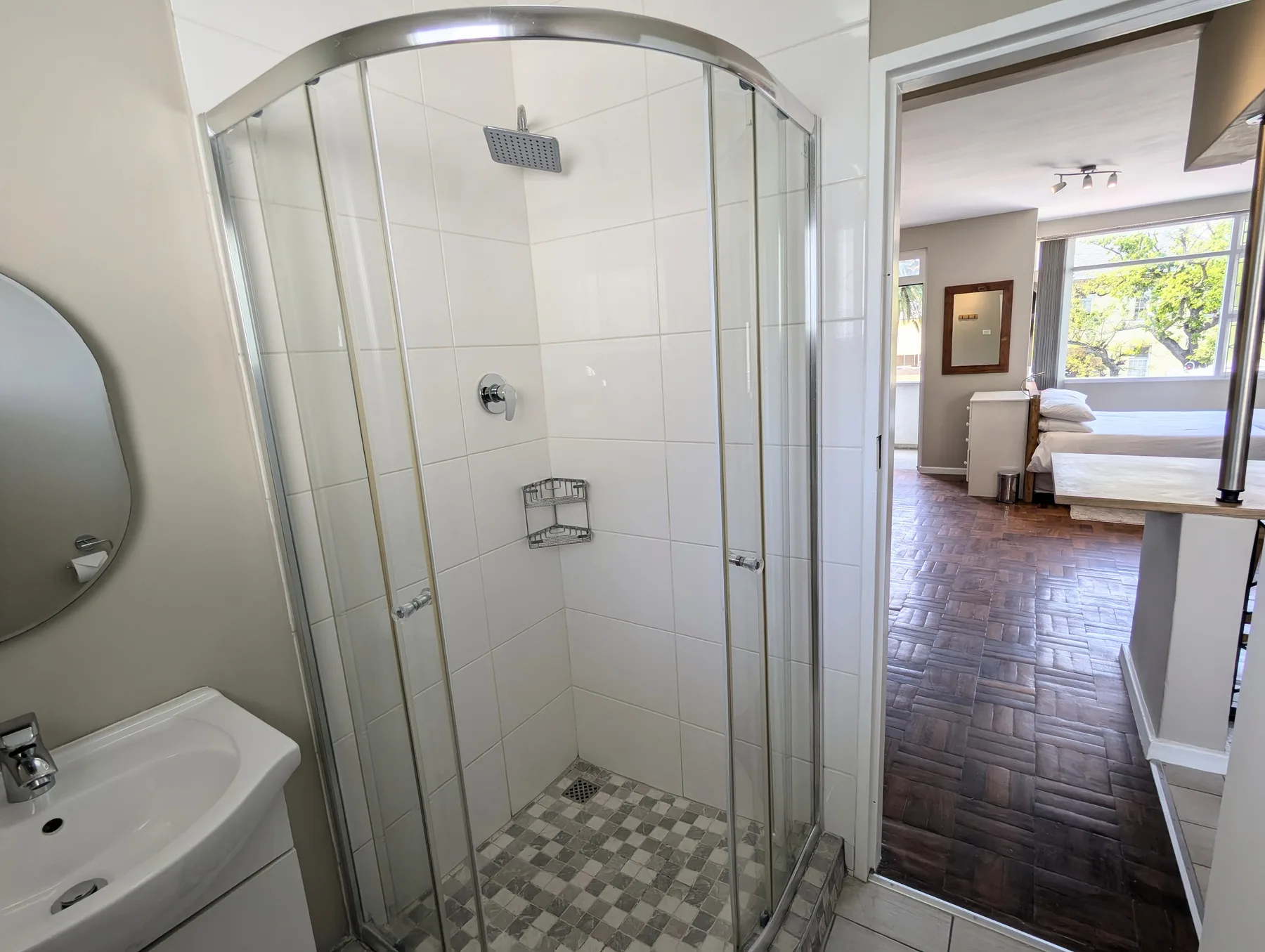 A tiled bathroom with a glass shower and a sink beside an open doorway.