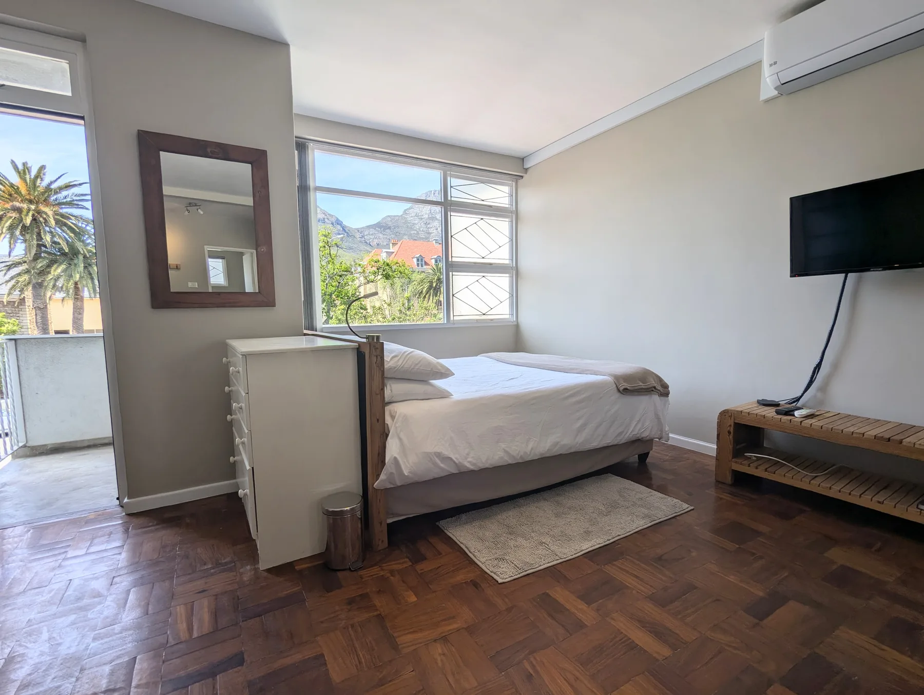 Un dormitorio luminoso con una cama, ventanas grandes y un televisor en la pared.