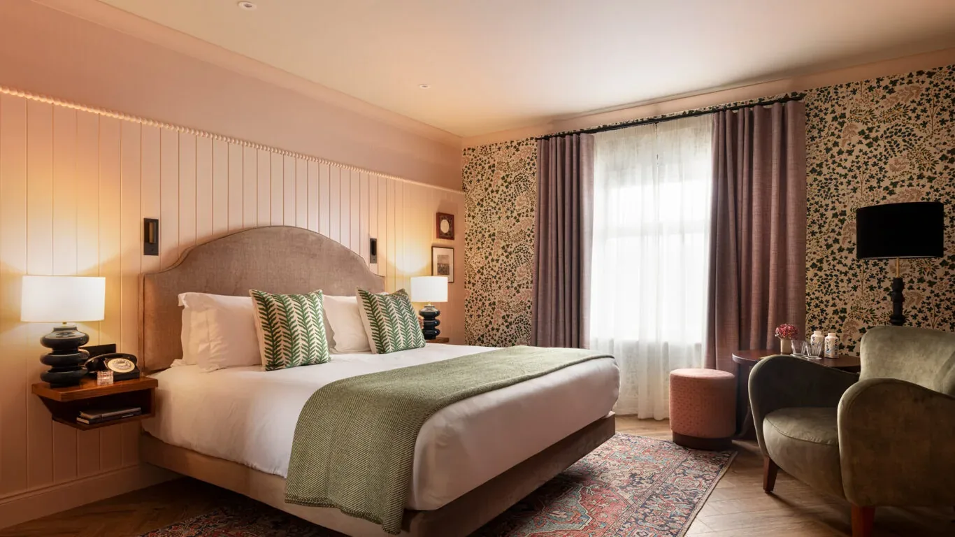 Habitación de hotel con una cama king size, un sillón y cortinas.