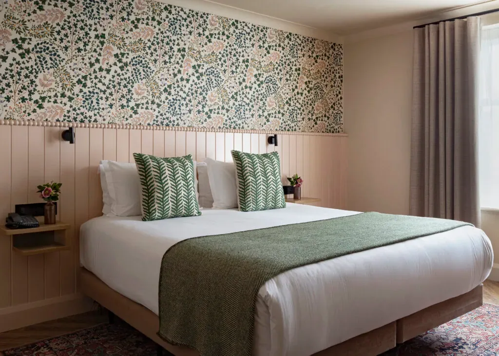 Habitación de hotel con una cama king size, detalles verdes y papel pintado floral.