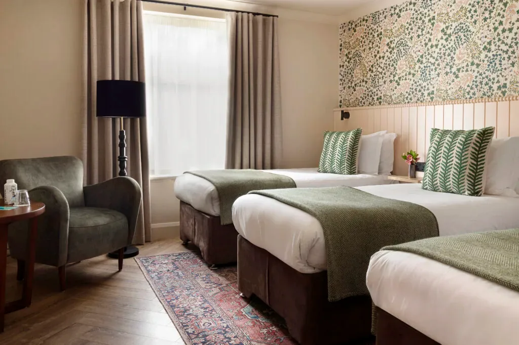 Habitación de hotel con tres camas, un sillón y papel pintado floral.