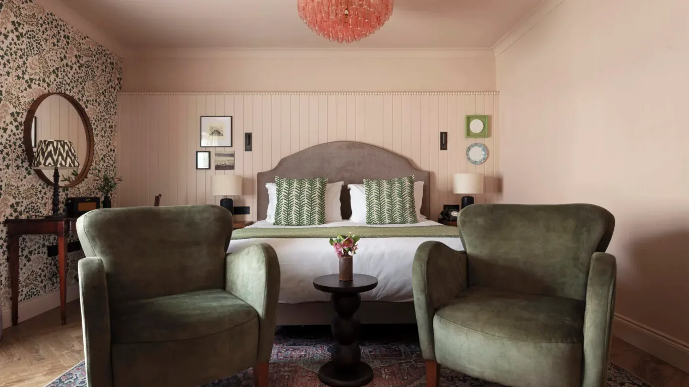 Habitación de hotel con sillas verdes, papel pintado floral y una cama.