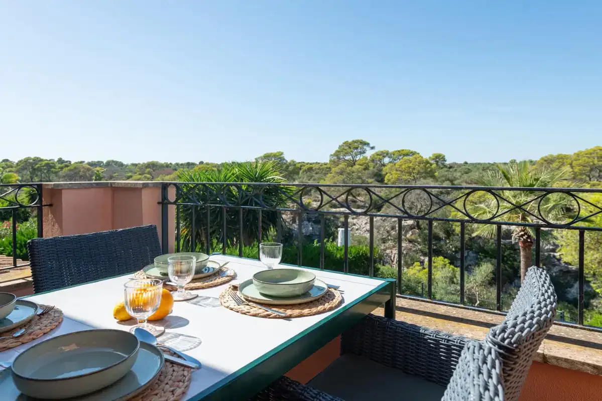 A balcony dining area overlooks a green landscape, with a table set for a meal.