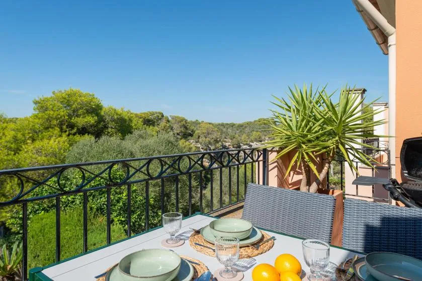An outdoor dining table sits on a terrace overlooking green trees.