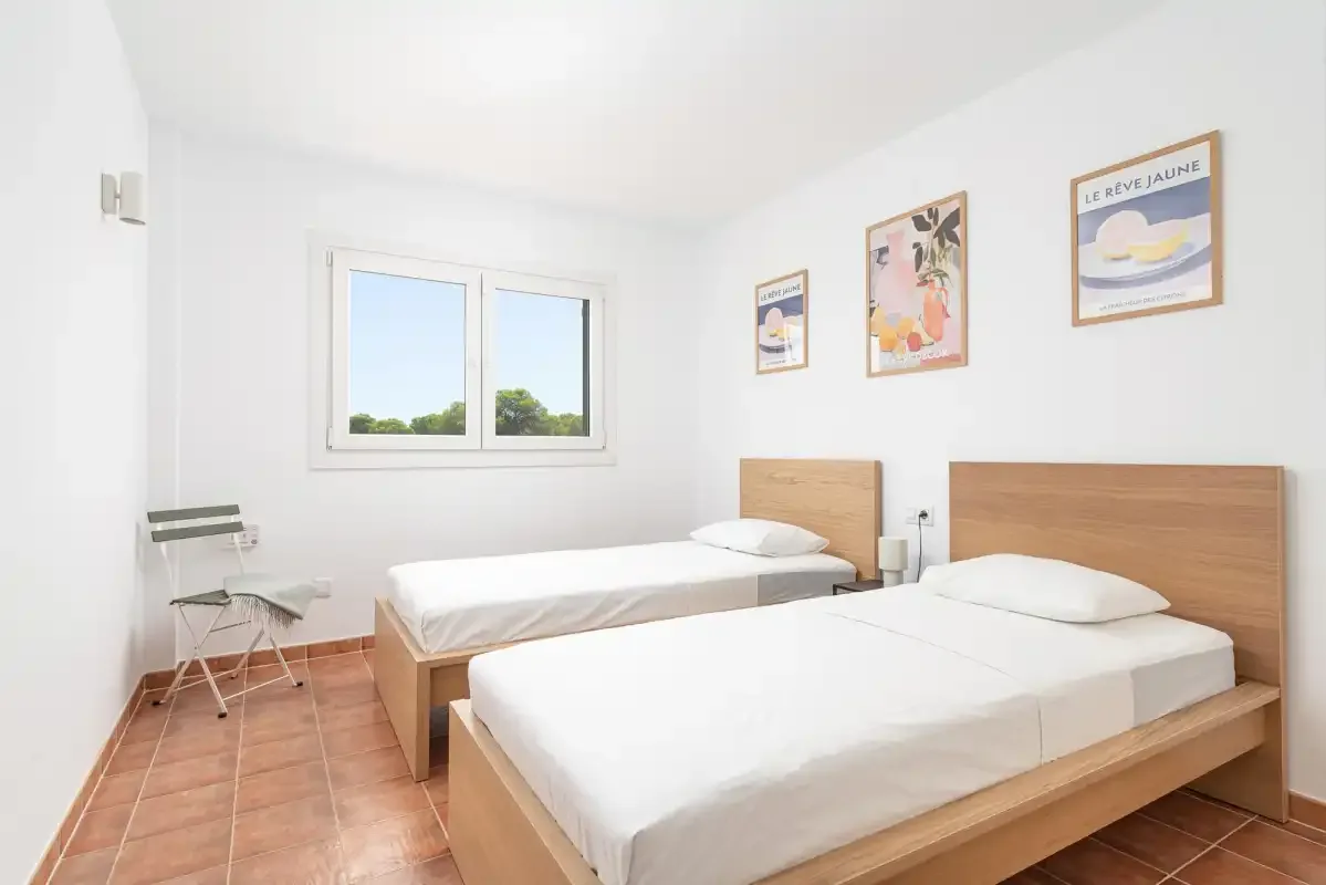 A bright bedroom with two beds and framed artwork on the wall.