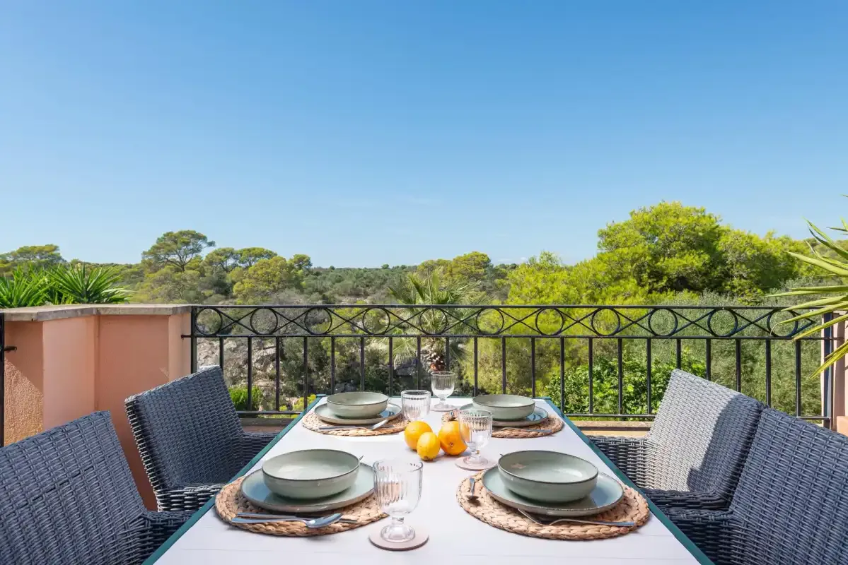 An outdoor dining table is set beside a railing overlooking trees.