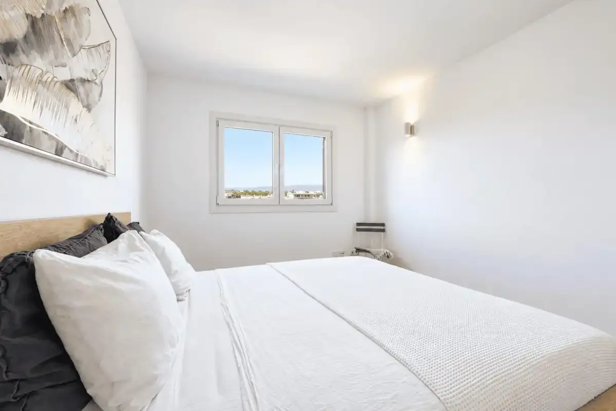 A bright bedroom with a neatly made bed and a window overlooking the landscape.