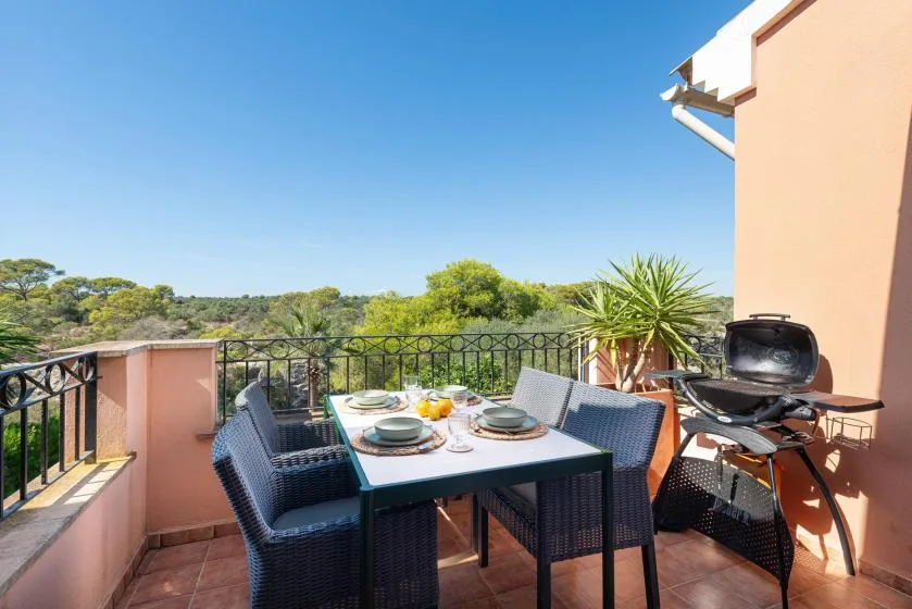 A rooftop terrace has an outdoor dining table, seating, and a grill beside a railing.
