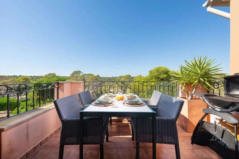 A terrace dining area has a table set beside a black railing.