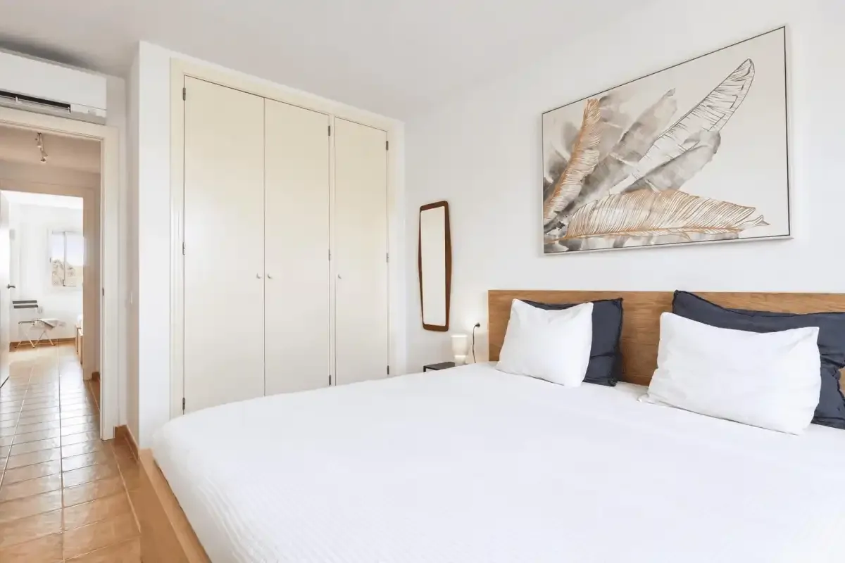 A bedroom with a bed, white bedding, and a large framed feather print.