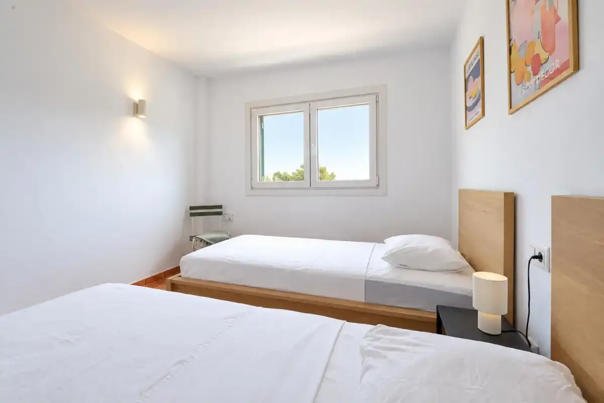 A bright bedroom with two beds and a window.