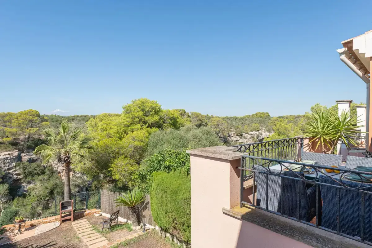 A terrace overlooks a green, tree-covered landscape beneath a clear blue sky.