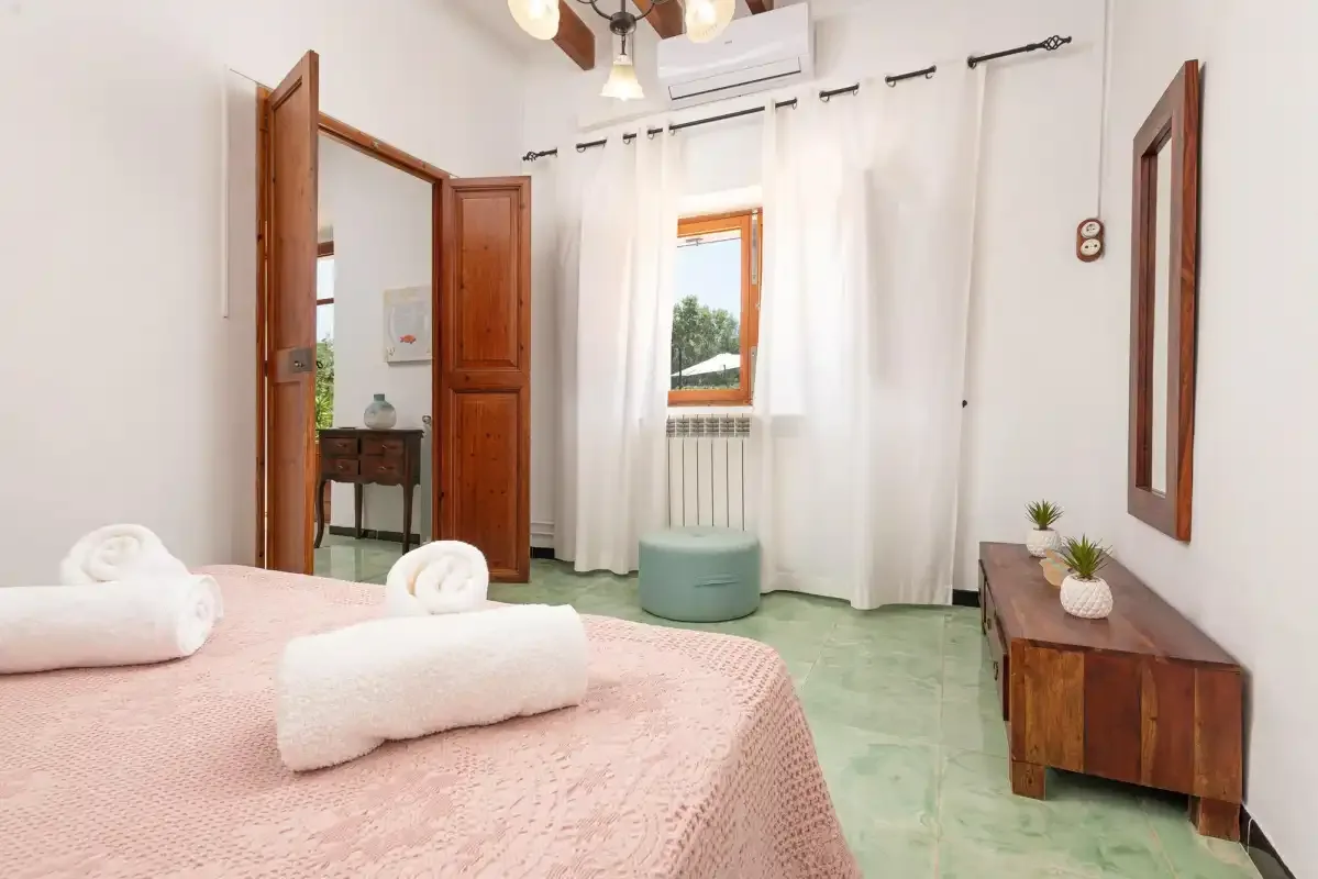 A bedroom with a bed, white curtains, and a small seating area by the window.