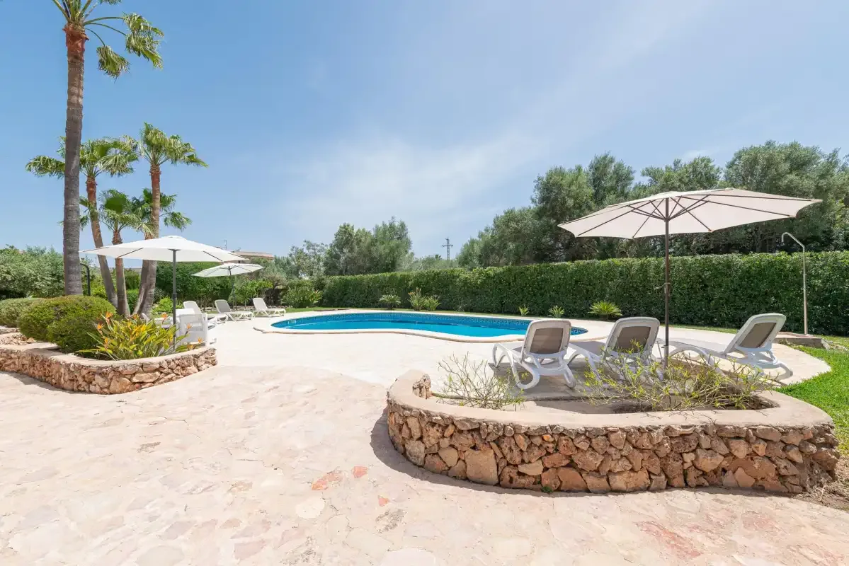 An outdoor swimming pool sits beside a paved patio with lounge seating and umbrellas.