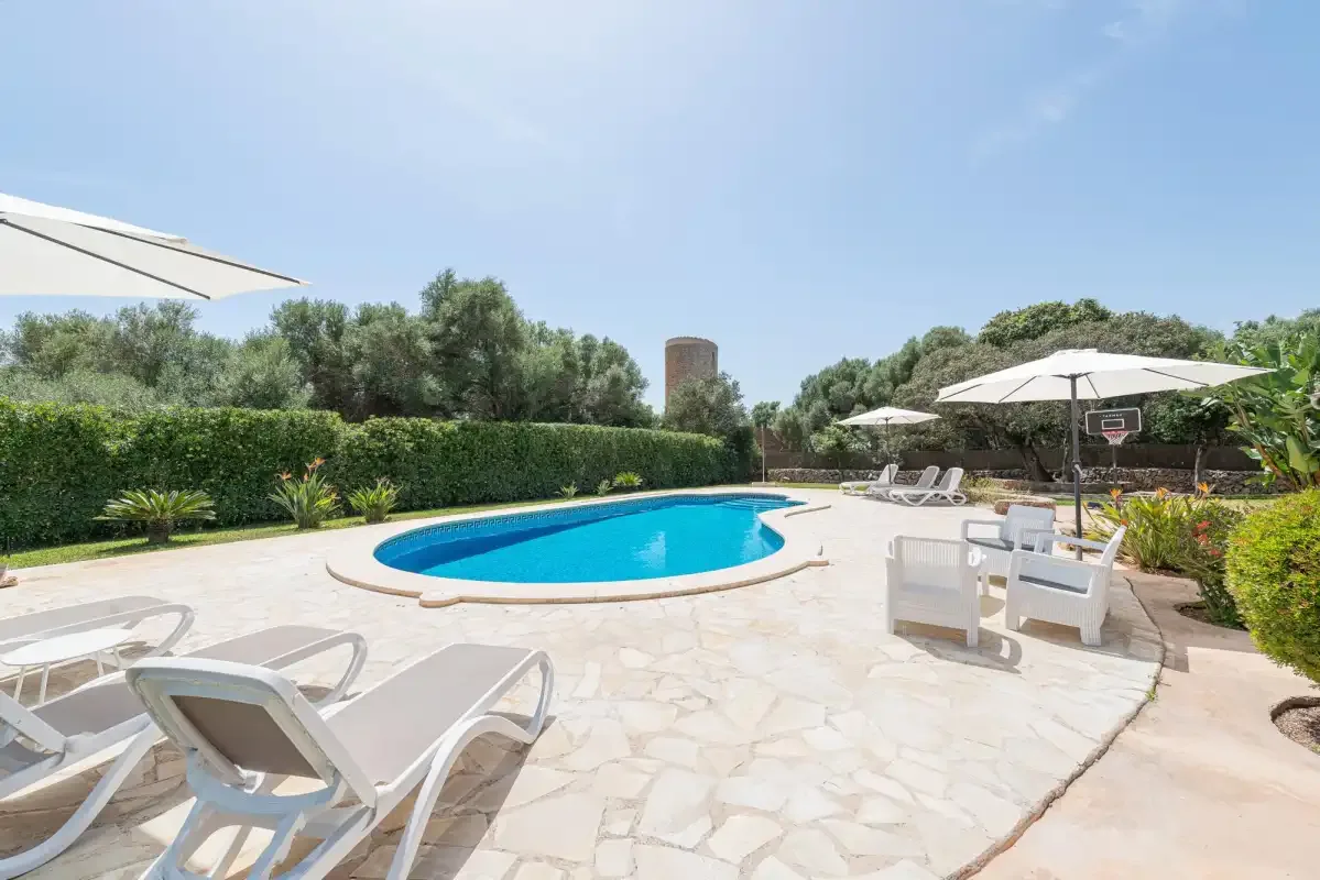 An outdoor swimming pool sits among pale paving, lounge seating, and greenery.