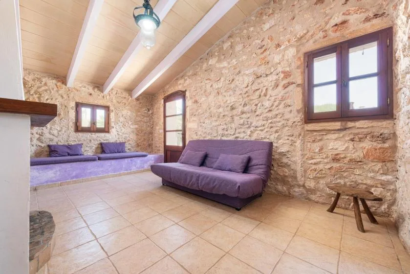 A stone-walled living room with purple seating and exposed ceiling beams.