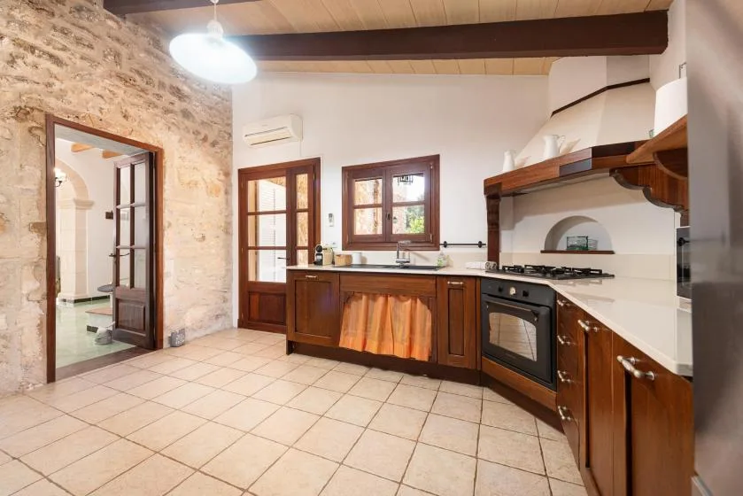 A spacious kitchen with dark wood cabinets, a tiled floor, and a stone wall.