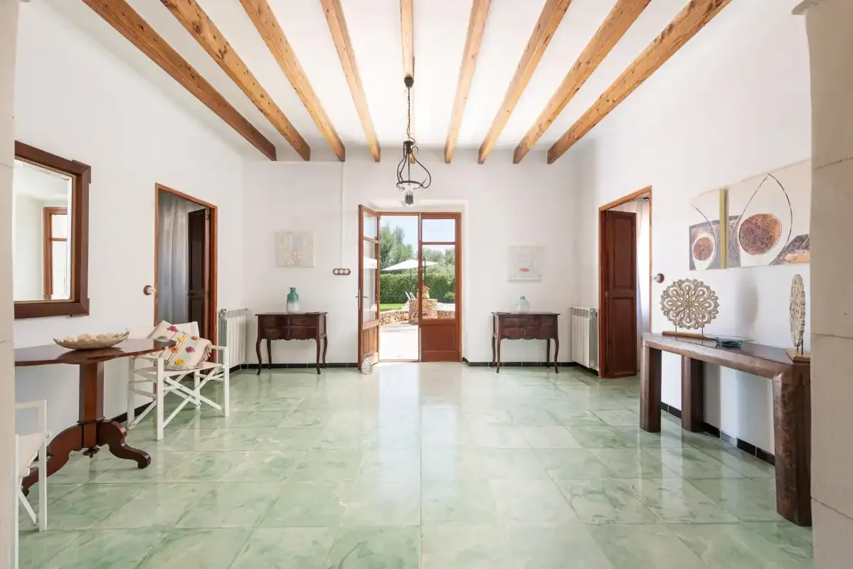 A bright room with wooden ceiling beams, tables, and doors opening to a garden.