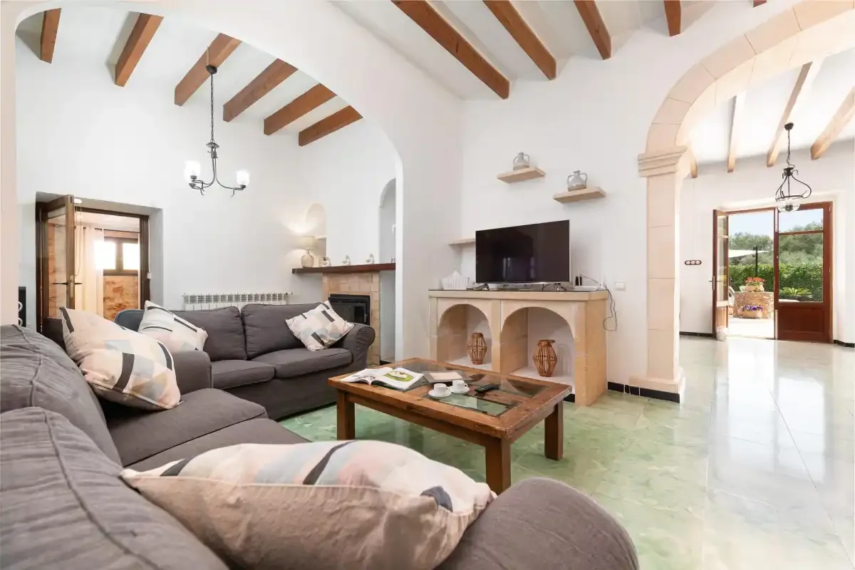 A bright living room with seating, a television, and exposed ceiling beams.
