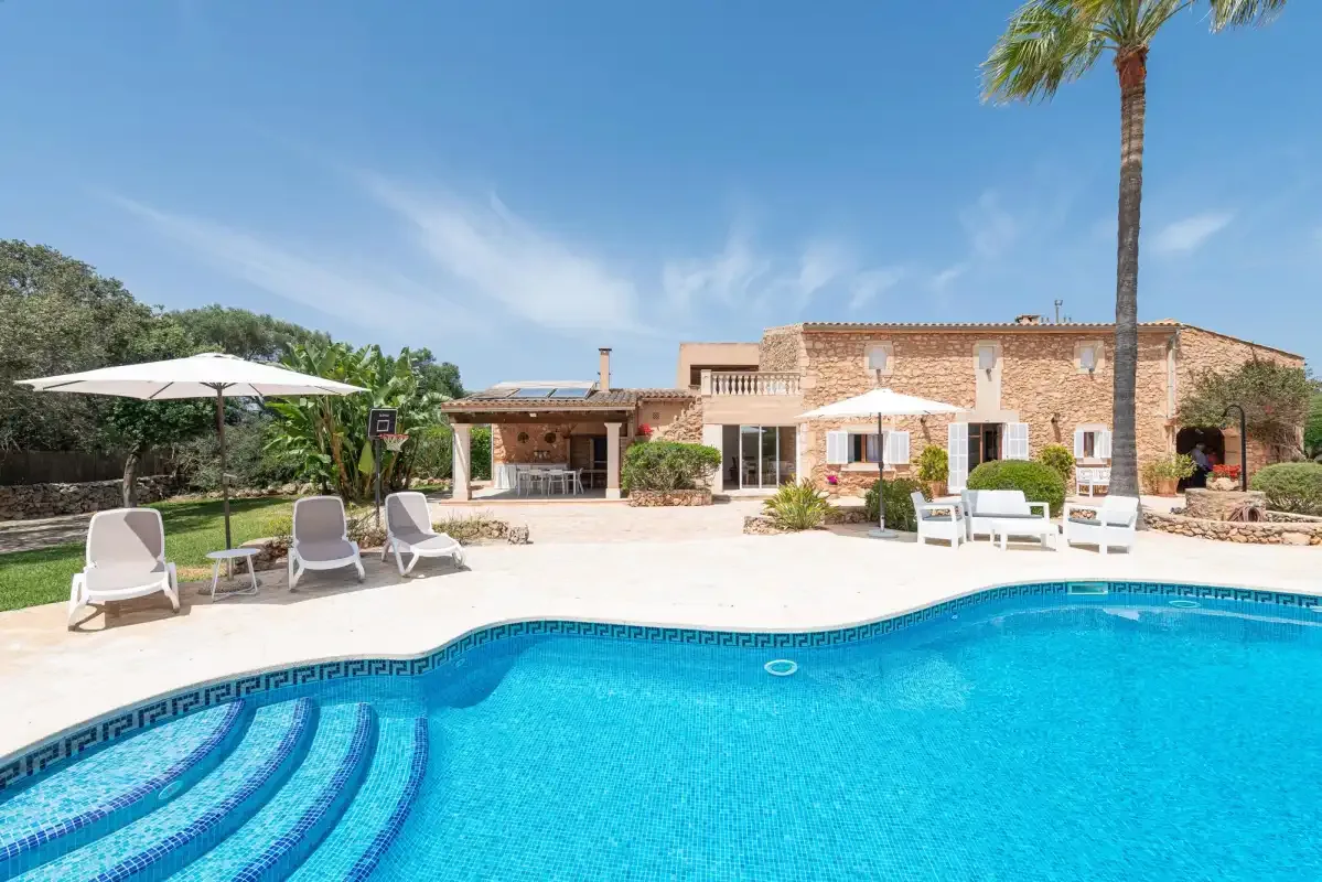A swimming pool and sun loungers sit in front of a stone house.